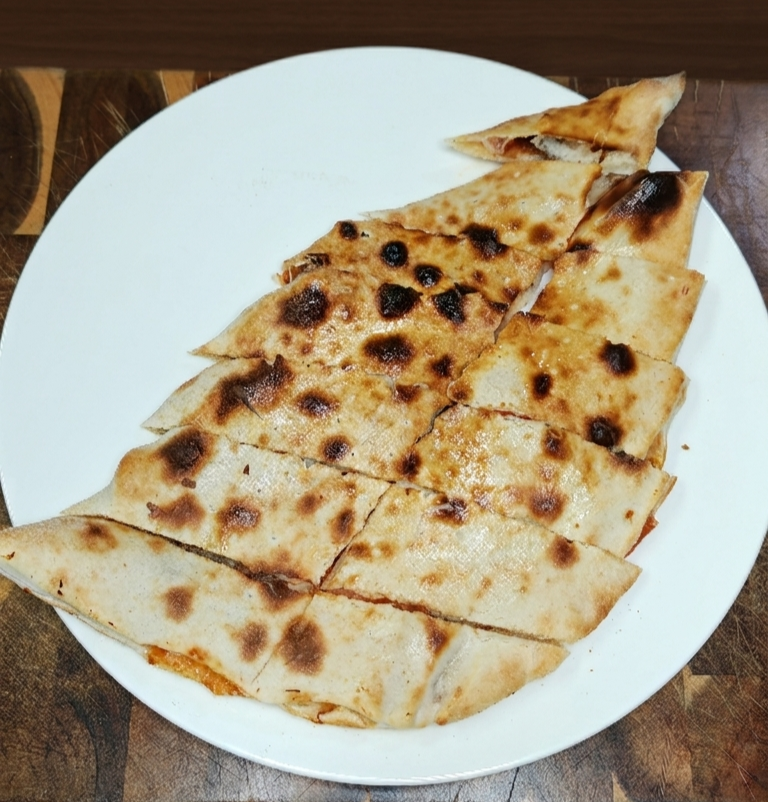 Eine weiße Platte mit mehreren Stückchen Fladenbrot, leicht gebräunt und mit dunklen Flecken, auf einem Holztisch.