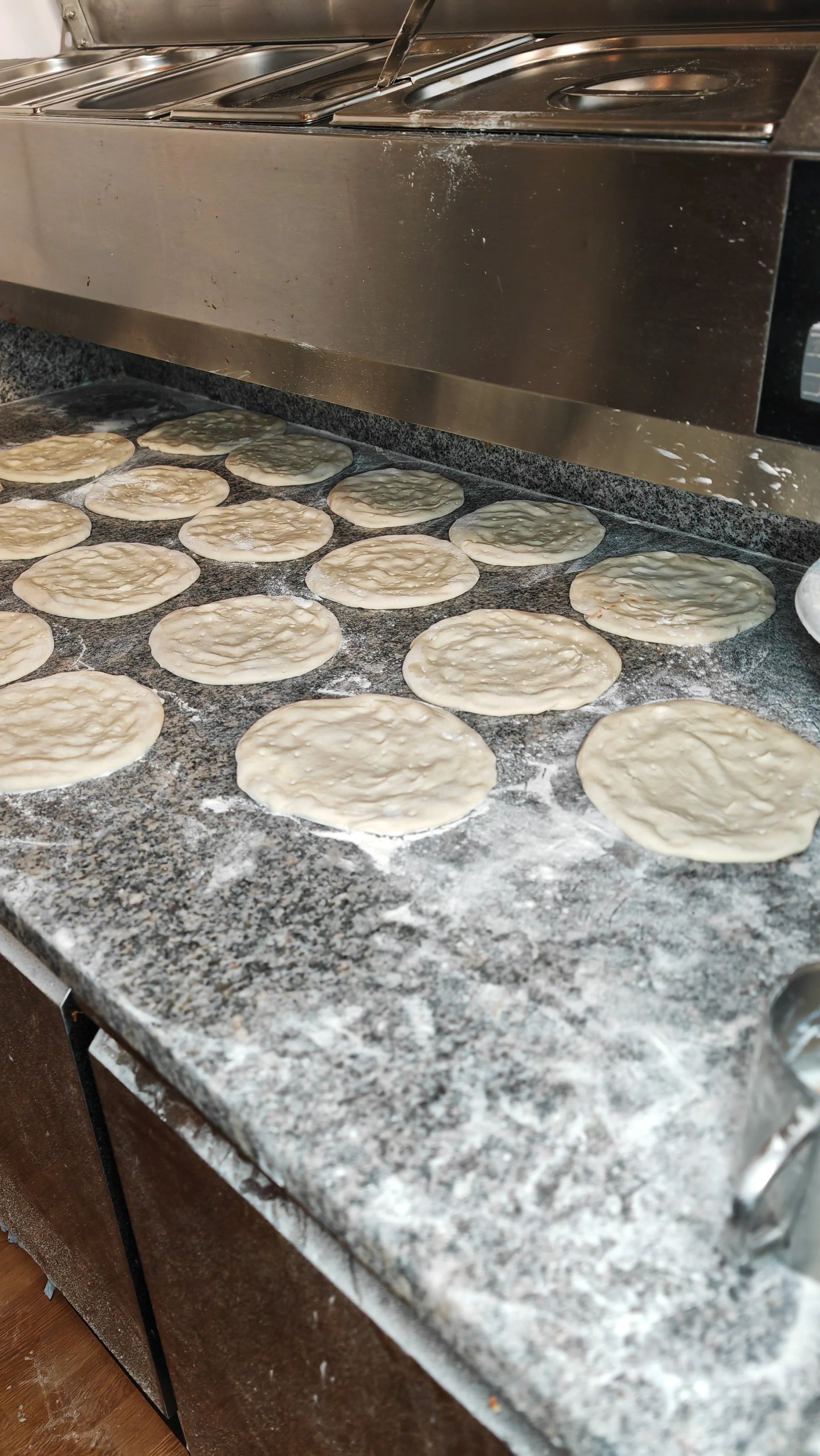 Kreise aus Teig werden auf eine bemehlte Küchenplatte gelegt, während ein Ofen im Hintergrund sichtbar ist.