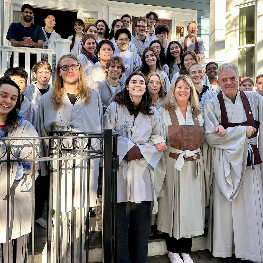 Group of people dressed in traditional medical or culinary attire standing on steps outside a house.