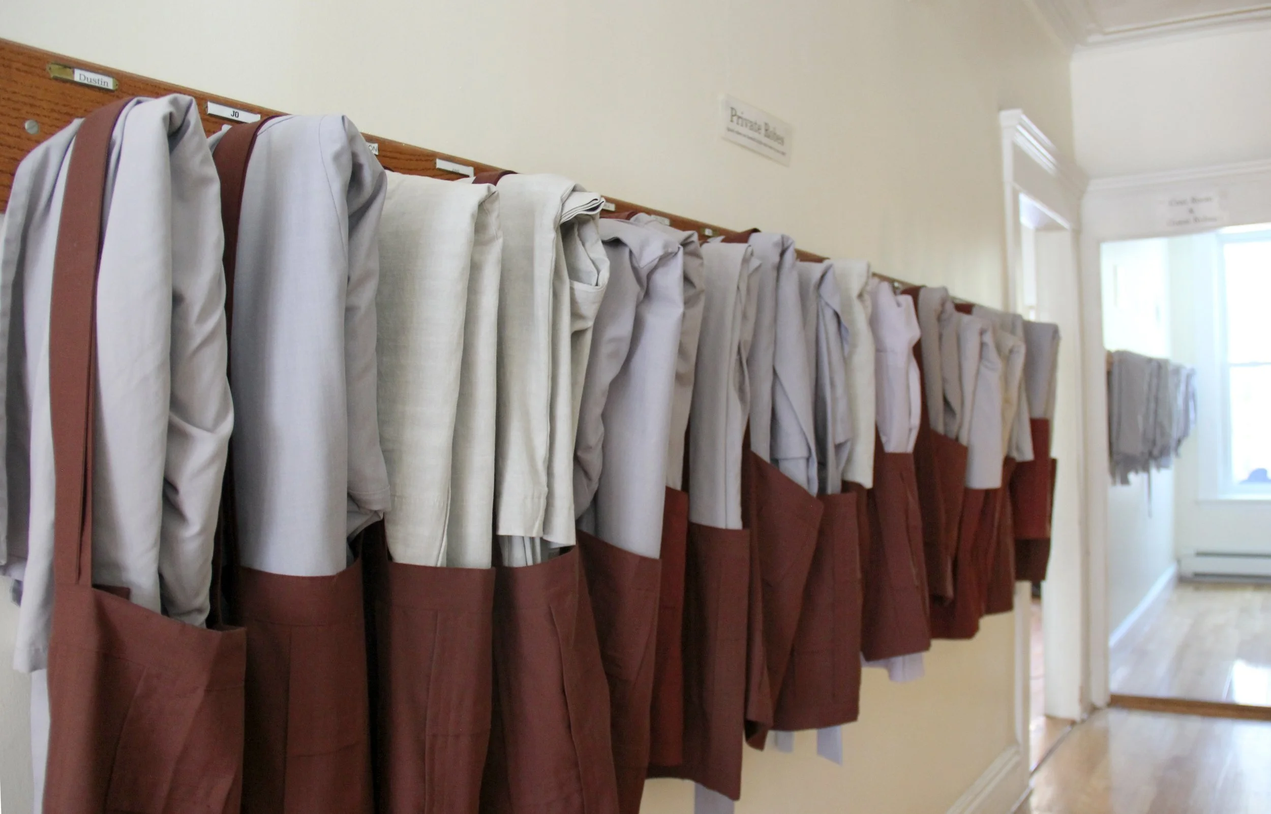 Clothes hanging on wooden hooks on a wall with labels for each. A door with a sign reading 'Private Room' and a window letting in natural light.