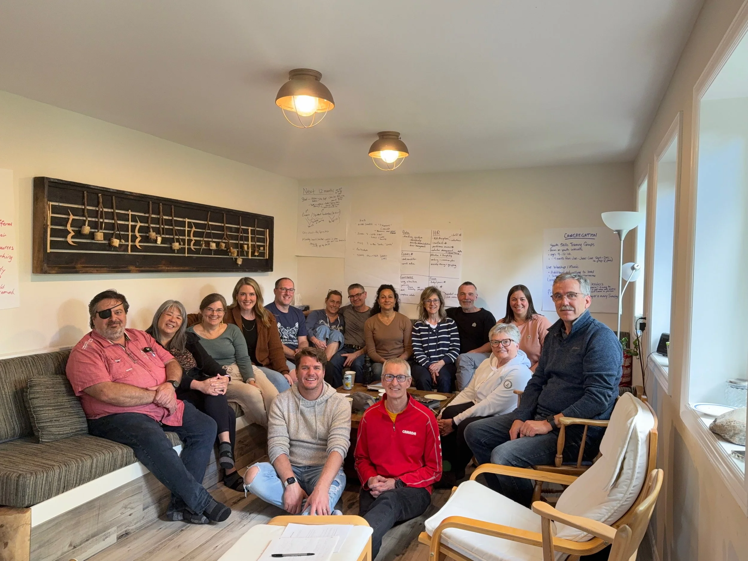Group of people sitting and smiling in a cozy living room with wall art and written notes on the wall.