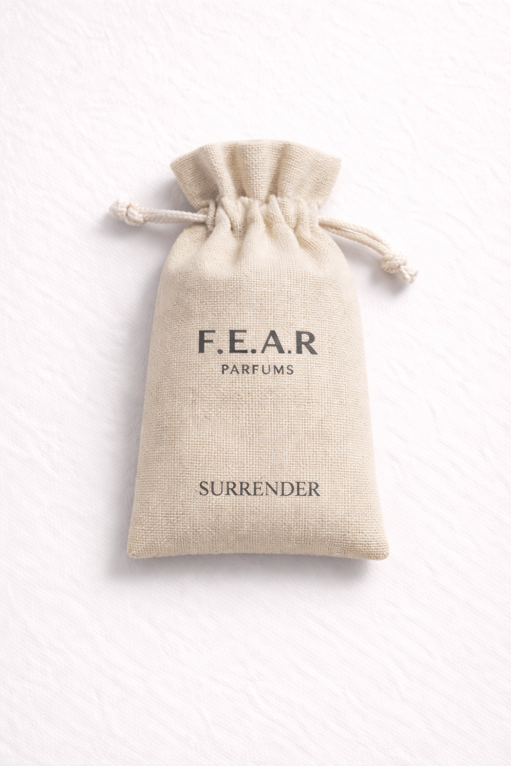 A beige fabric pouch with a drawstring closure, labeled 'F.E.A.R PARFUMS SURRENDER' on a white background.