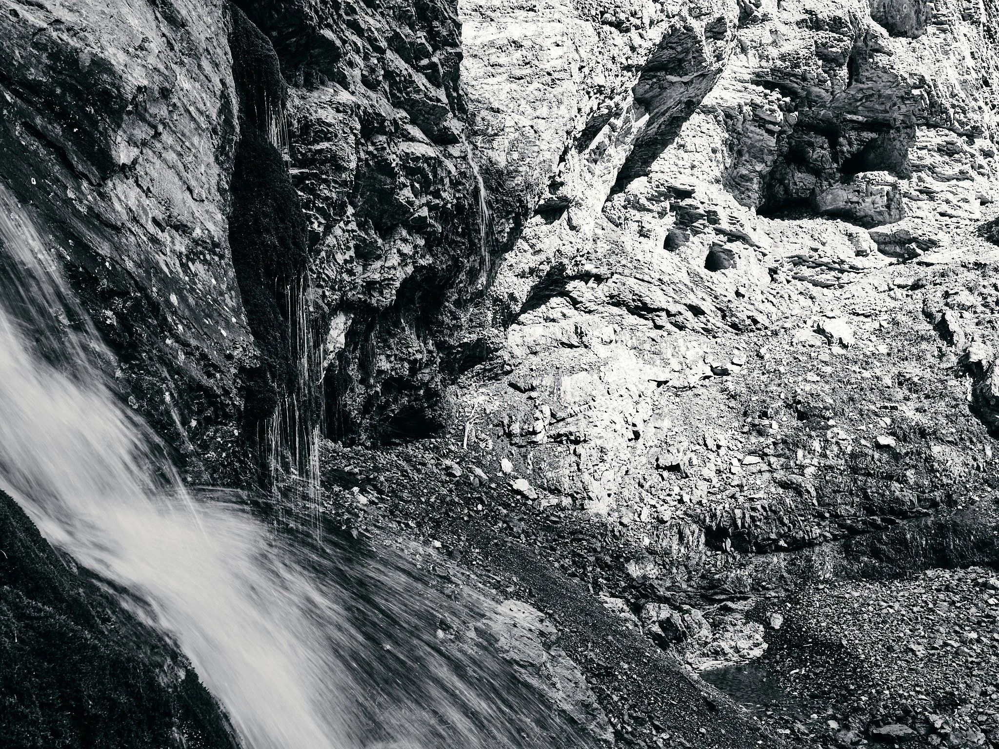 Black and white photo of a mountainside with rocks and a waterfall flowing at the left side.