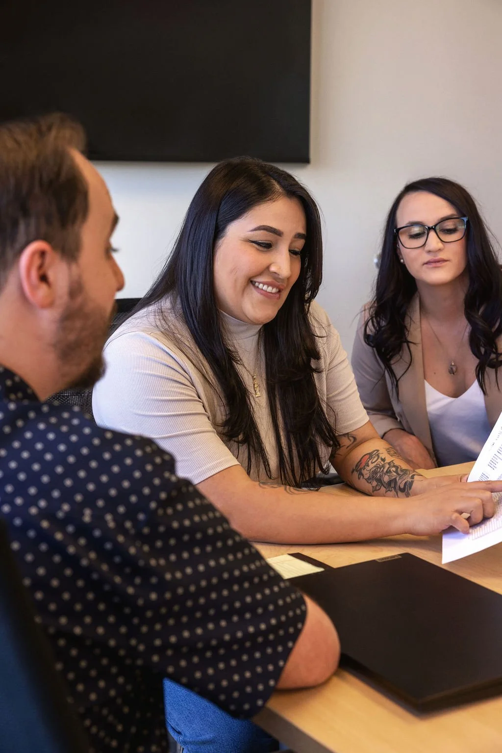 Three people sitting at a table in a meeting, two women and one man, with documents and a laptop.