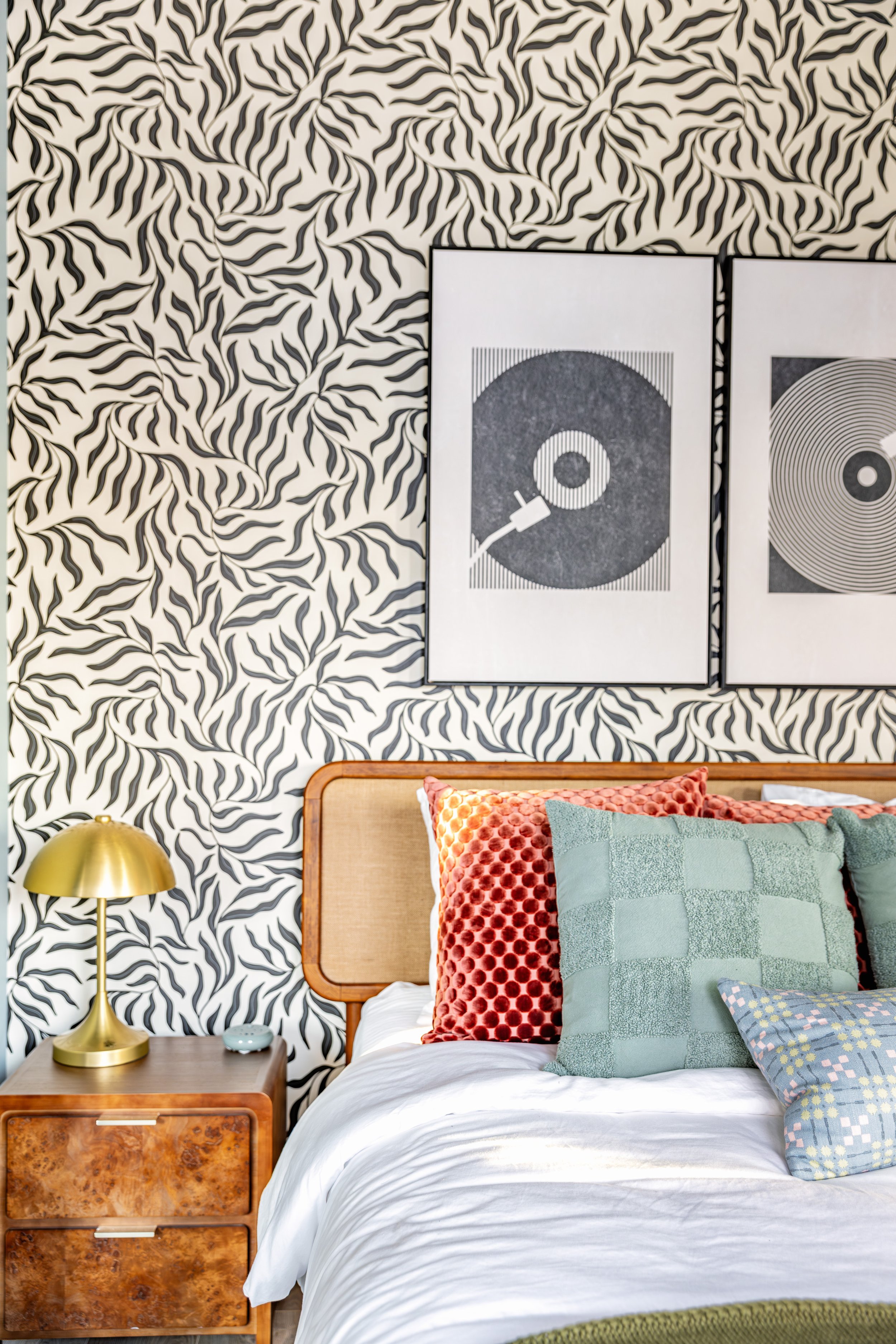 A bedroom with a zebra print wallpaper, a wooden bed with colorful pillows, and two black and white art prints of turntables on the wall.