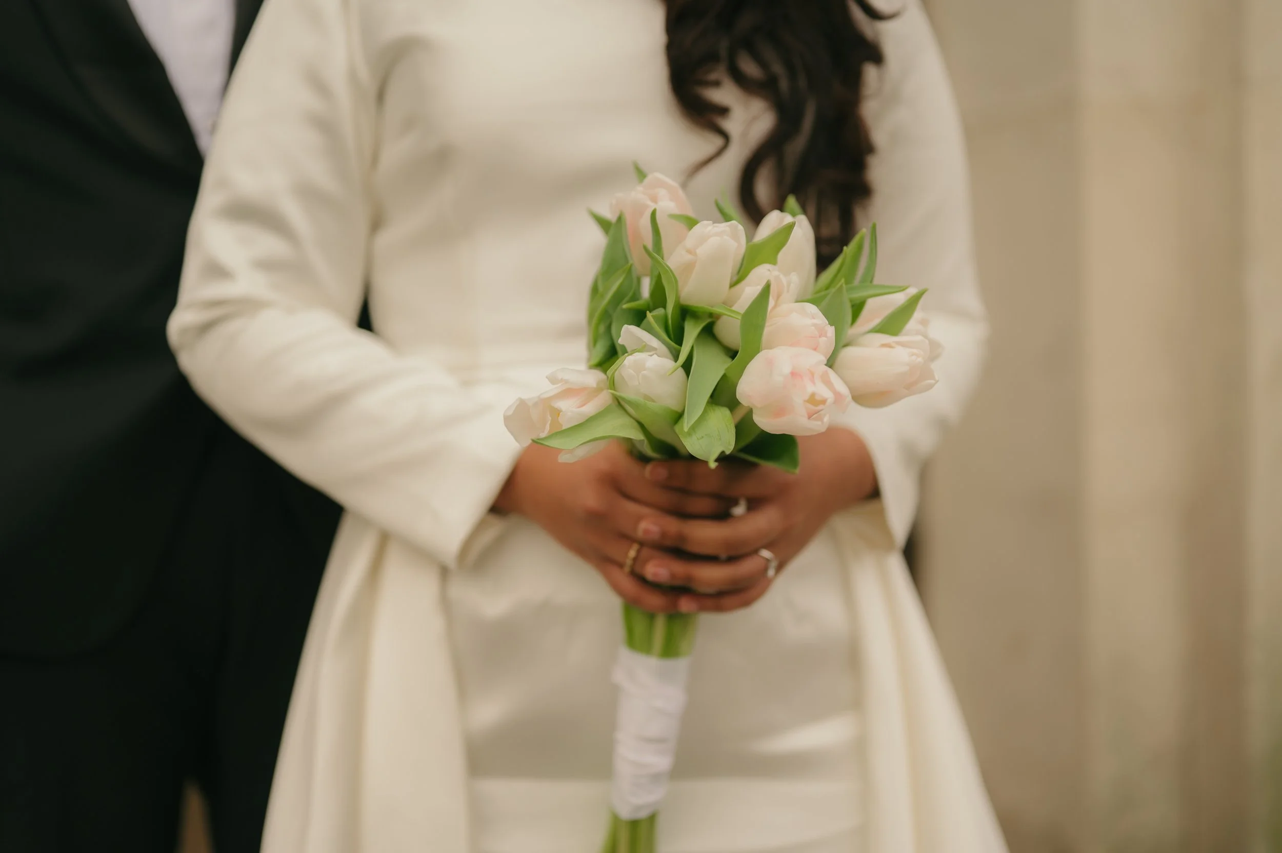 A woman in a white dress holding a bouquet of light pink tulips with green leaves.