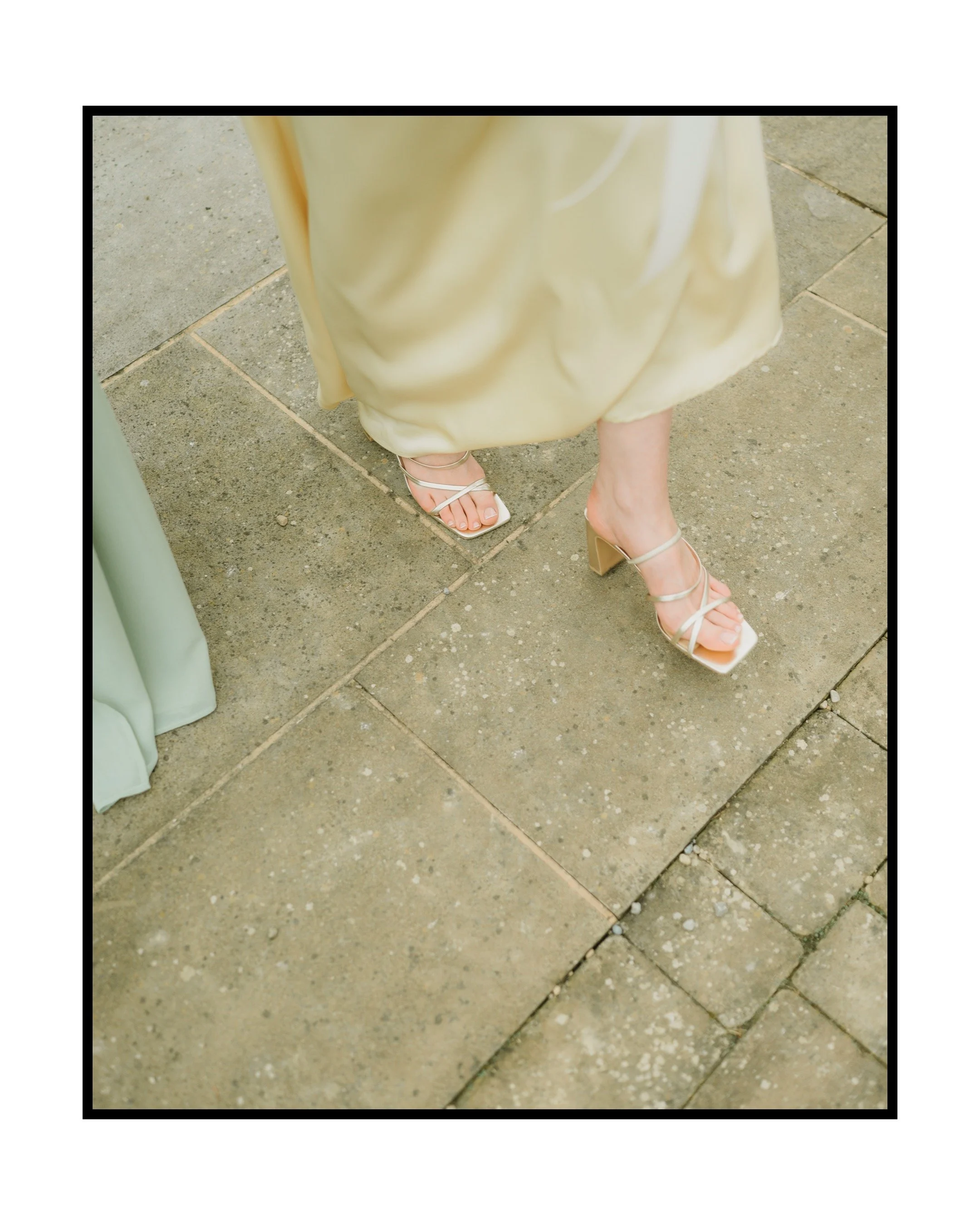 Close-up of a woman wearing beige heels and a flowing yellow dress, standing on stone pavement.