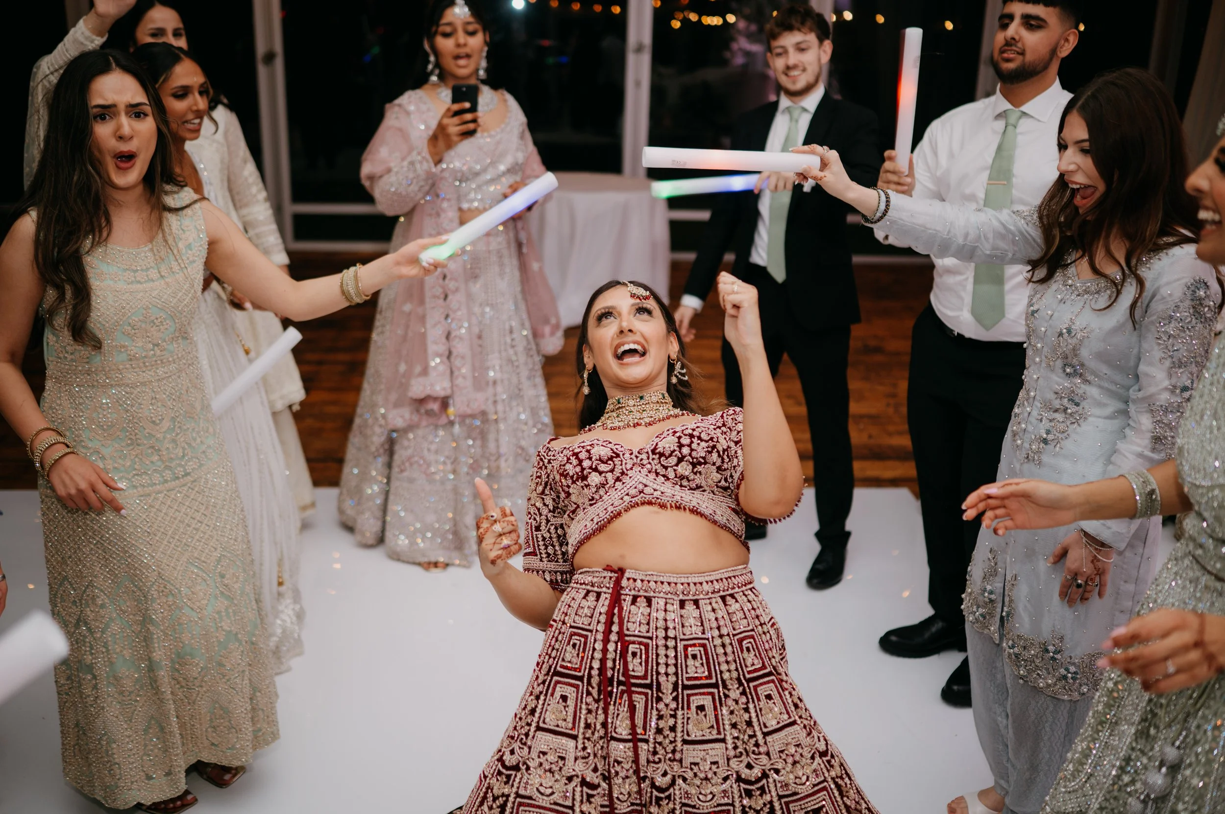Group of women and men celebrating at a wedding, ring light sticks, and a woman in traditional Indian attire dancing.
