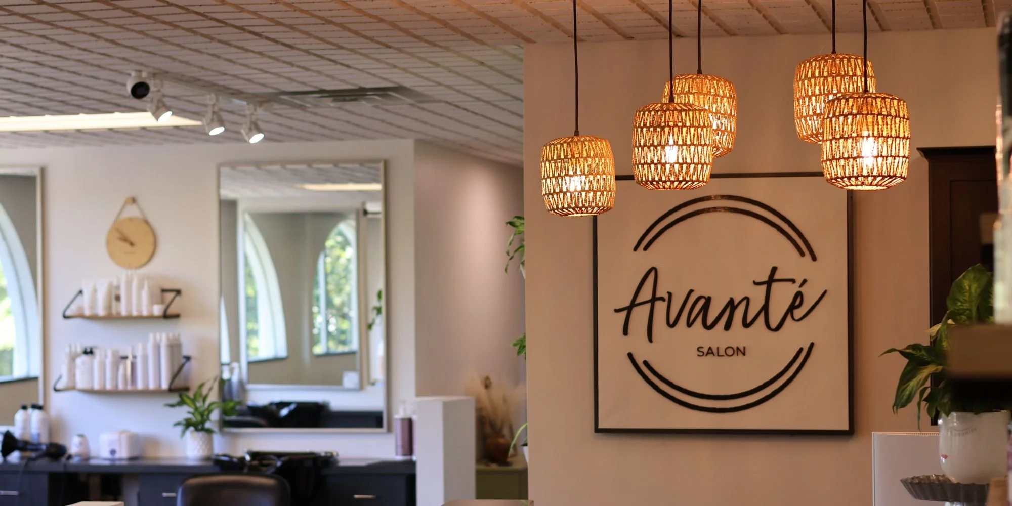 Interior of a salon with hanging rattan pendant lights and a sign that reads "Avanté Salon" on the wall.