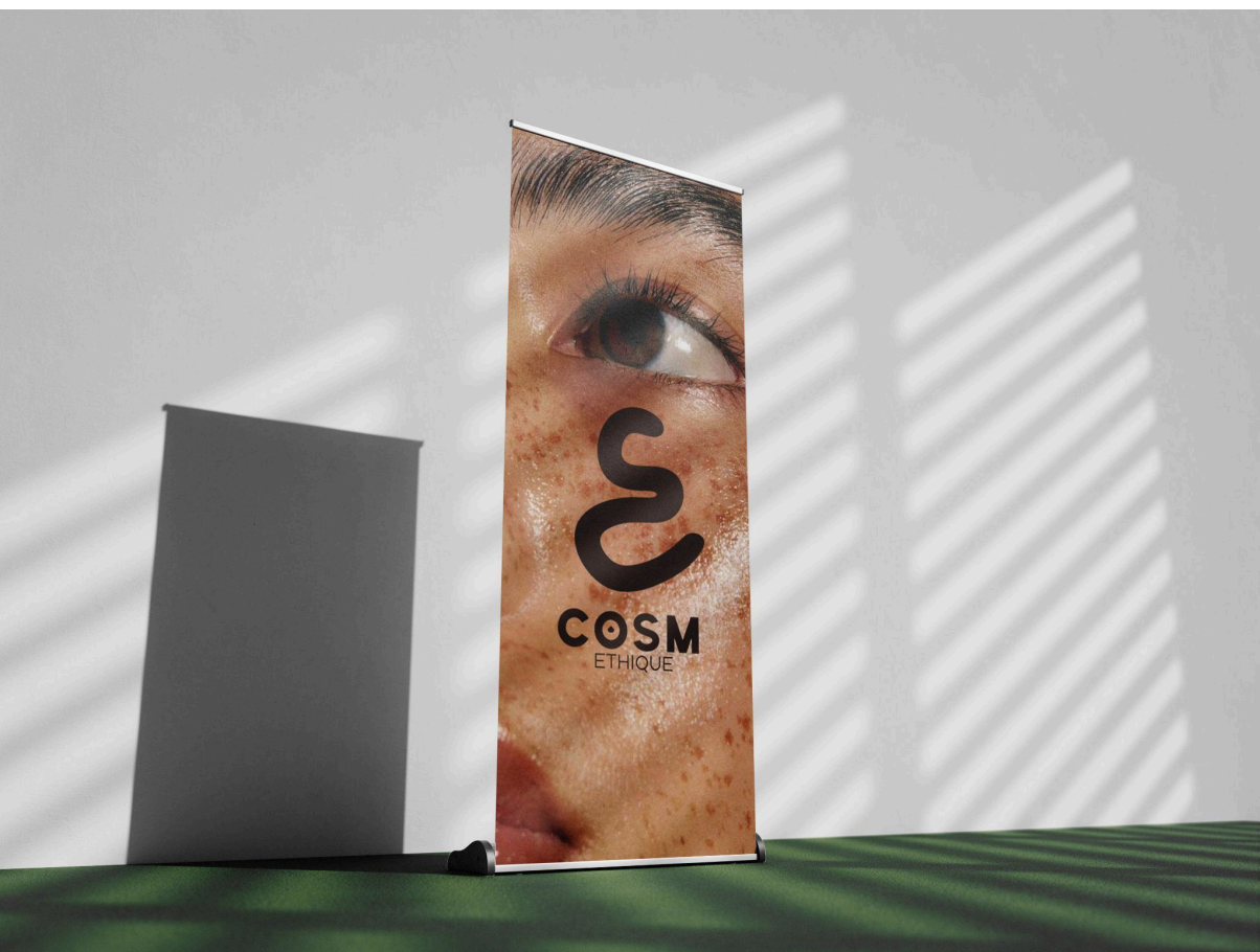 Une bannière publicitaire avec un gros plan d'un visage à la peau marquée de taches de rousseur, notamment autour de l'œil. La bannière affiche le texte 'COSM ETHIQUE', avec un symbole en forme de 'S' stylisé.