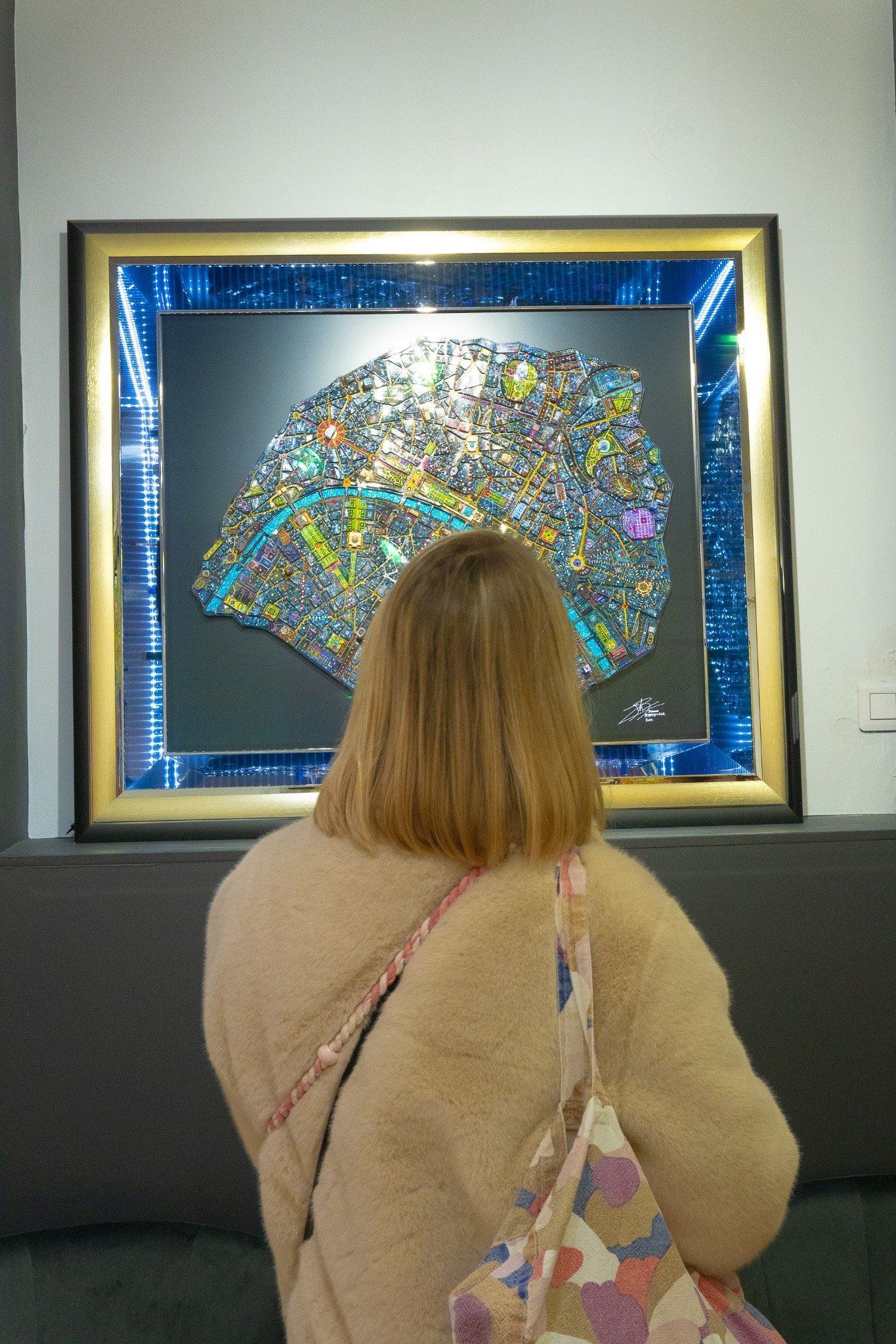 Une femme regarde une œuvre d'art colorée et complexe dans un cadre illuminé.