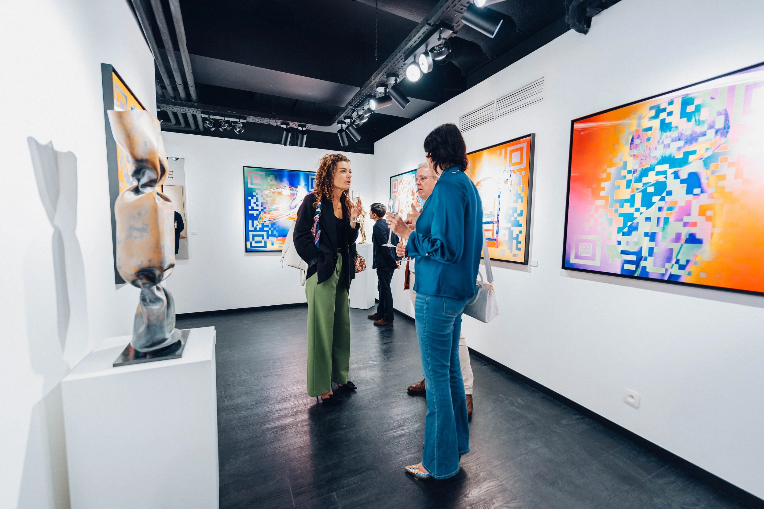 Groupe de personnes discutant dans une galerie d'art contemporain avec des œuvres colorées sur les murs.