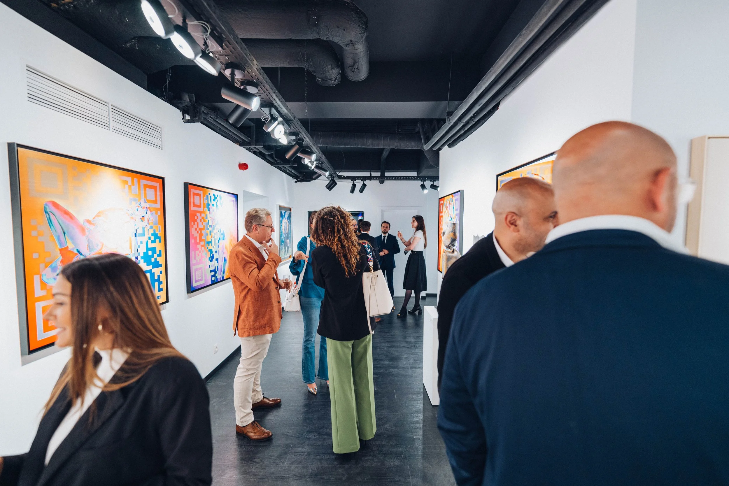 Visiteurs dans une galerie d'art regardant des œuvres numériques colorées sur des murs blancs dans un espace d'exposition moderne.