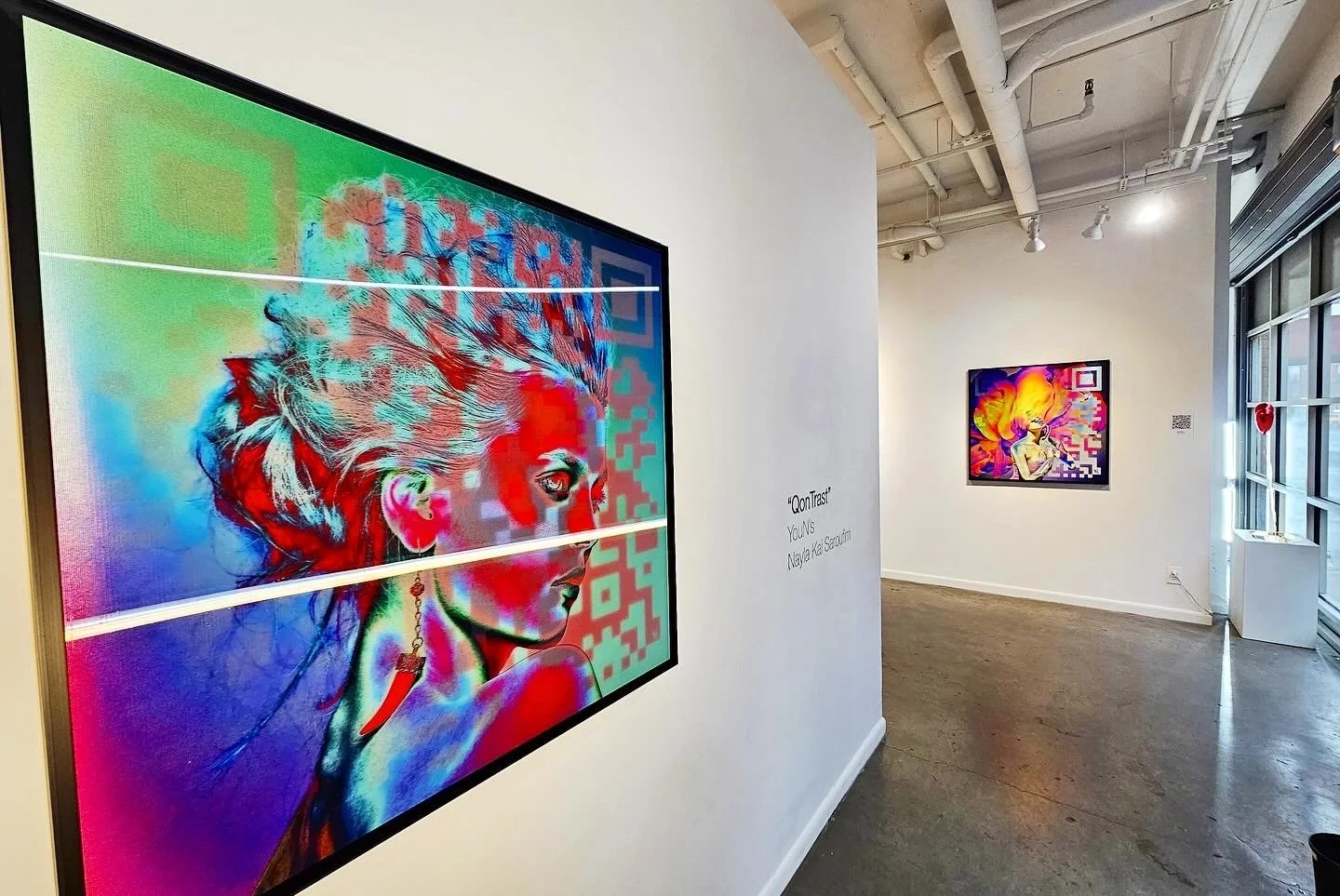 Exposition d'art avec deux œuvres numériques colorées, dont une de face de profil d'une femme avec des cheveux lumineux, dans une galerie
