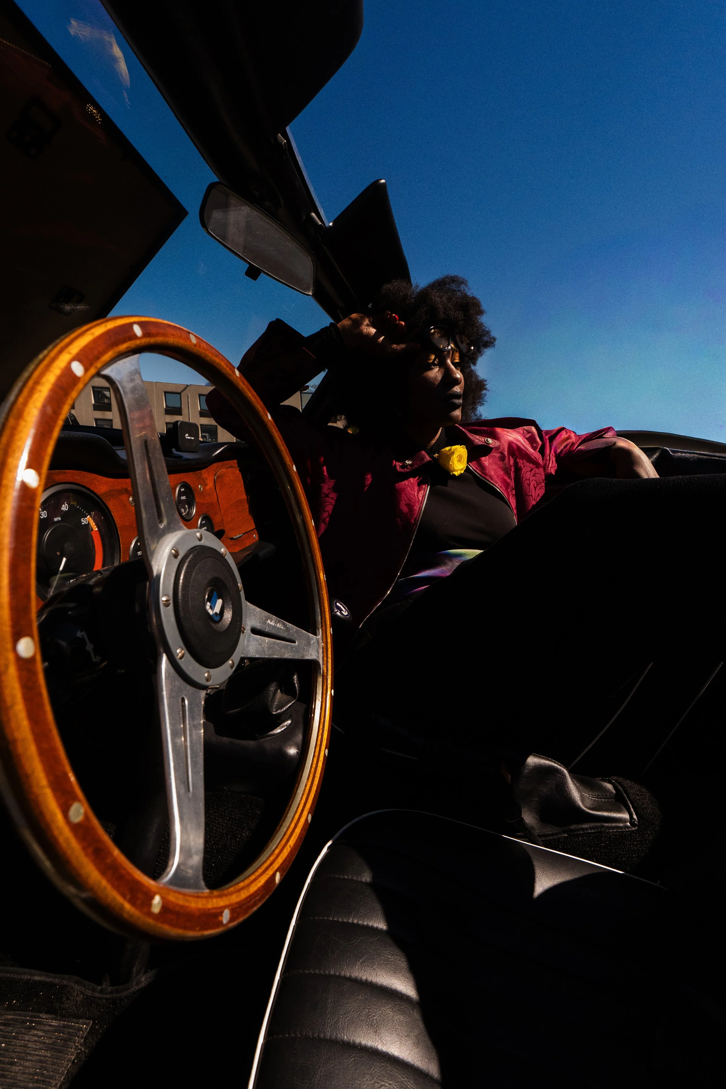 Une femme assise dans une voiture avec un tableau de bord en bois, sous un ciel bleu clair.