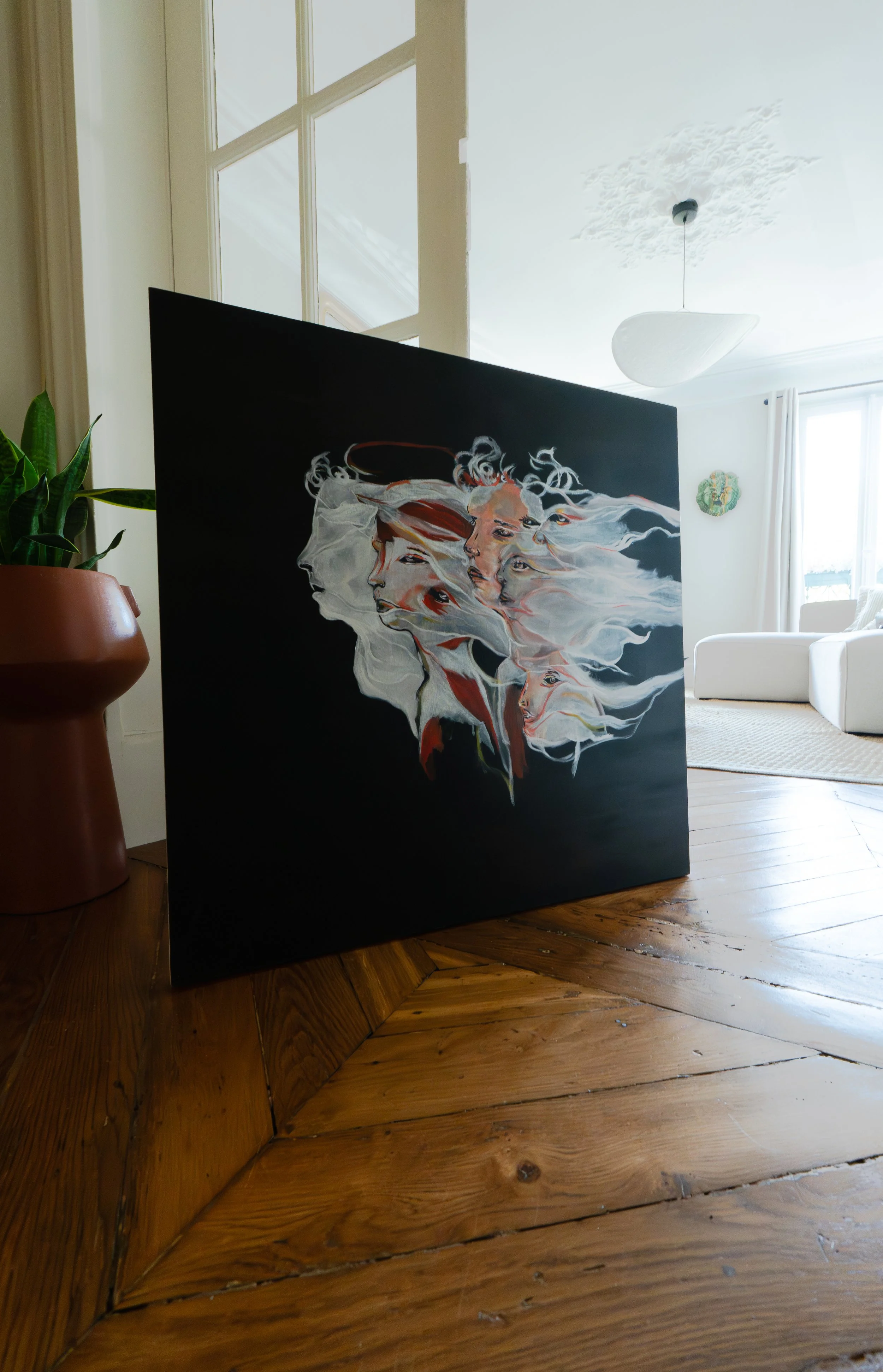 Une peinture abstraite représentant plusieurs visages féminins avec des cheveux flottants, installée dans un salon lumineux