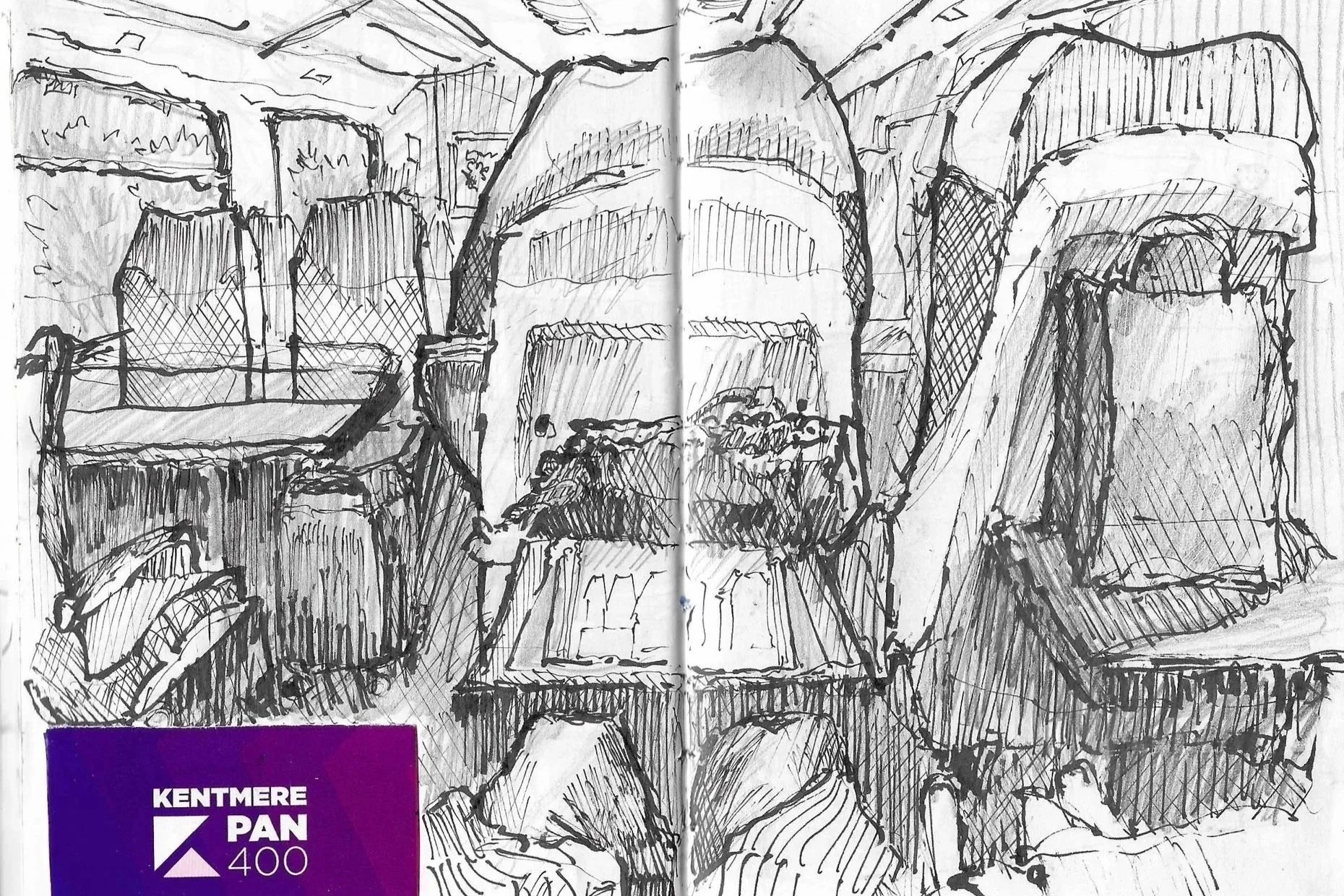 A sketch of a train's interior with multiple chairs and a table, viewed from the perspective of a person sitting, with the person's feet visible at the bottom of the image.