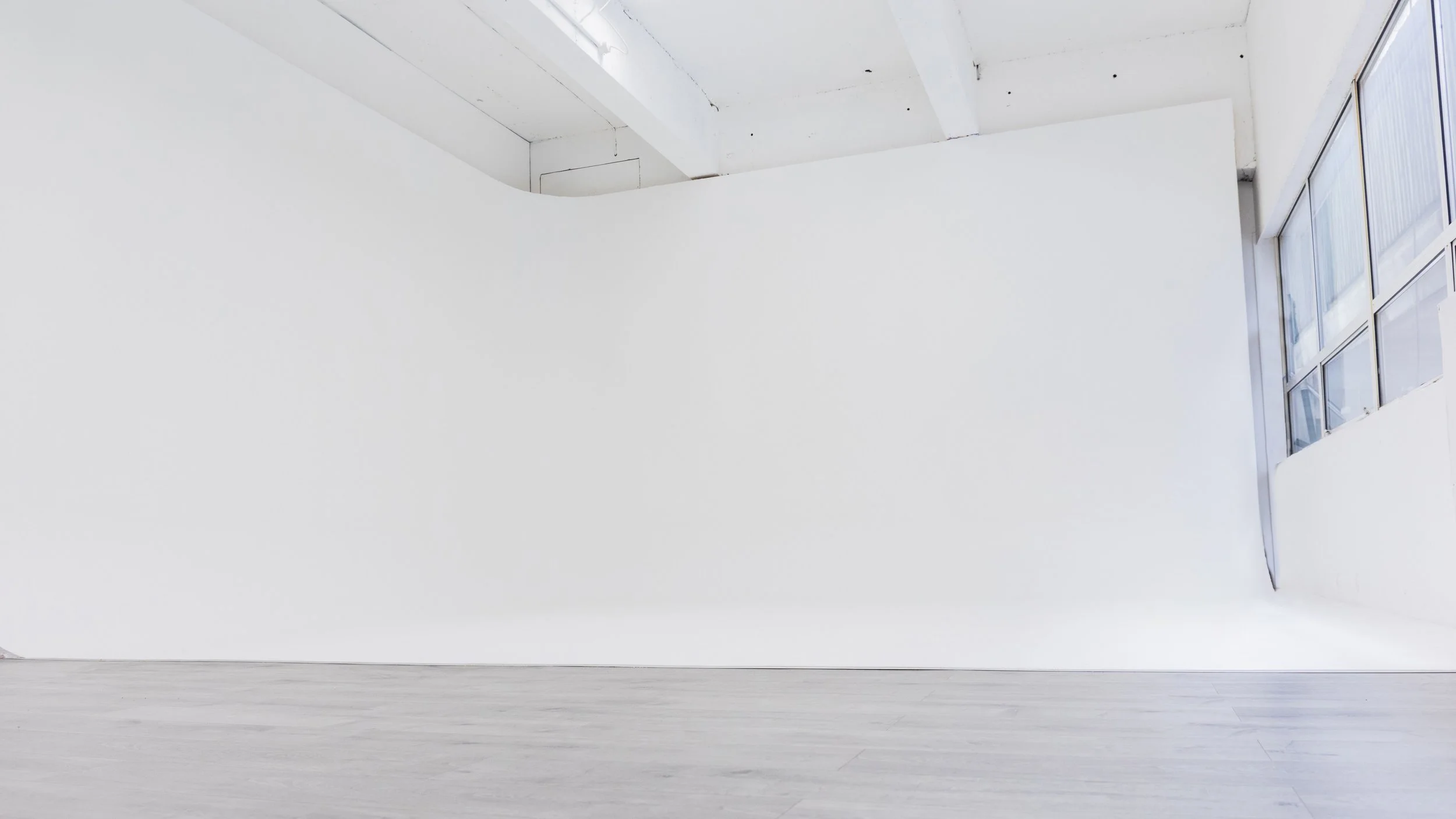 Empty white room with large windows on right side and natural light coming in.