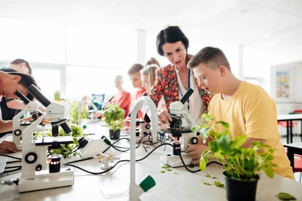 Teacher and students observing plants through microscopes in a classroom.