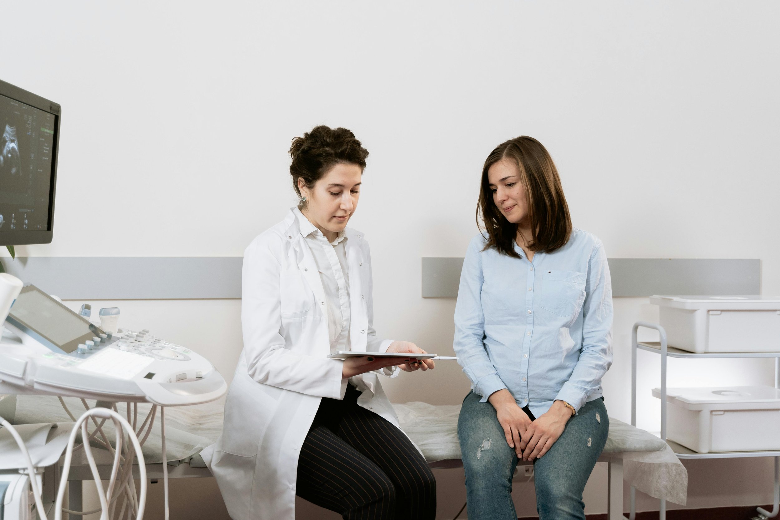 A female healthcare professional showing an ultrasound image to a female patient during a consultation in a medical examination room.