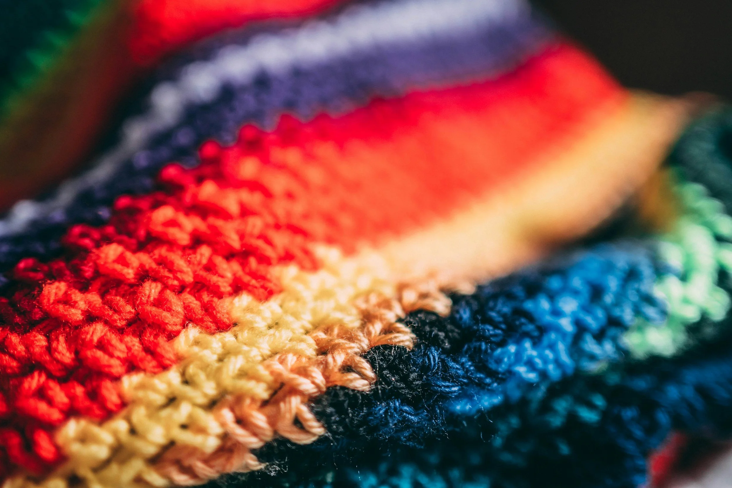 Close-up of a multicolored knitted fabric with horizontal stripes in red, yellow, navy blue, and green.