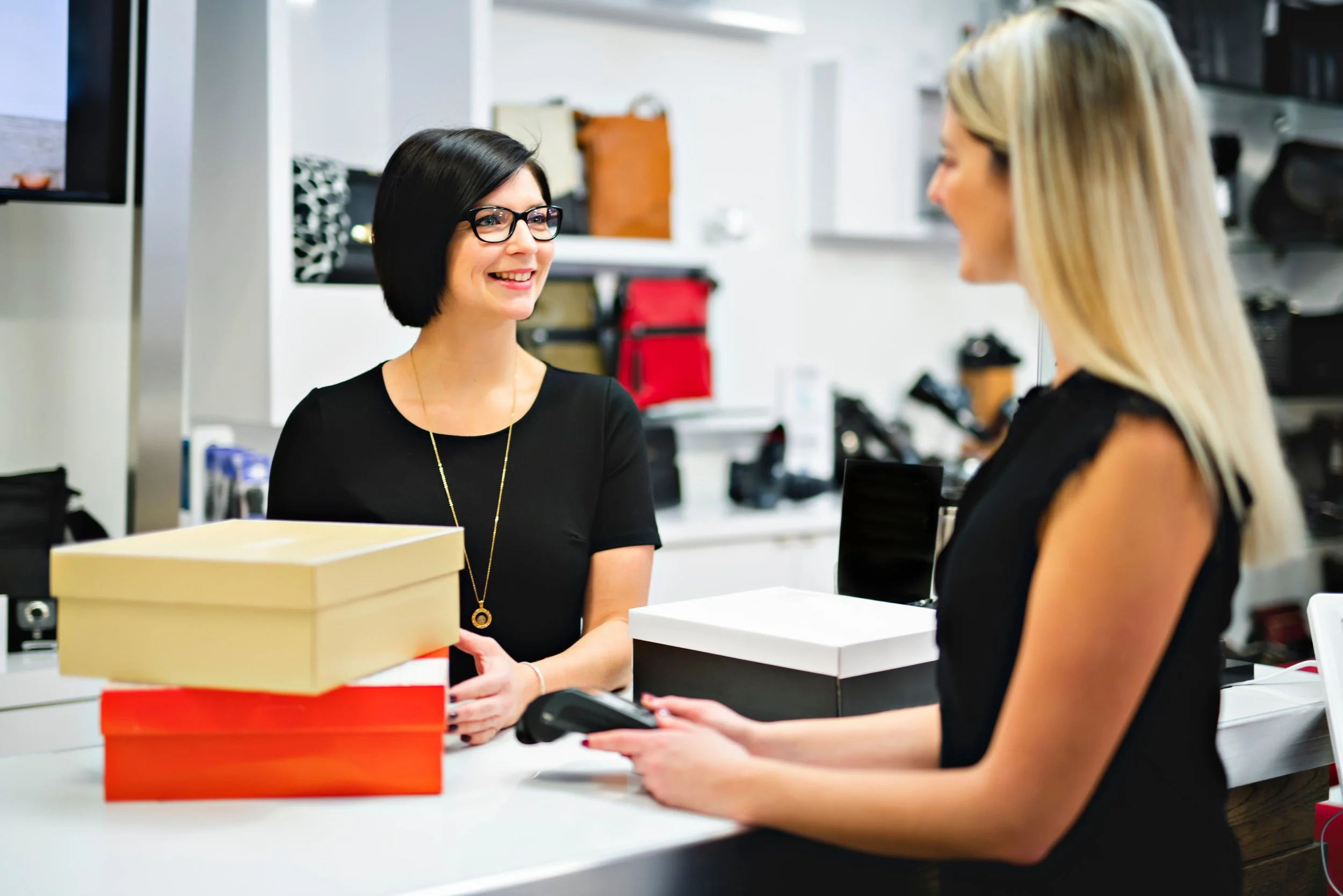 Two women at a checkout counter in a store, exchanging payment, with boxes on the counter.