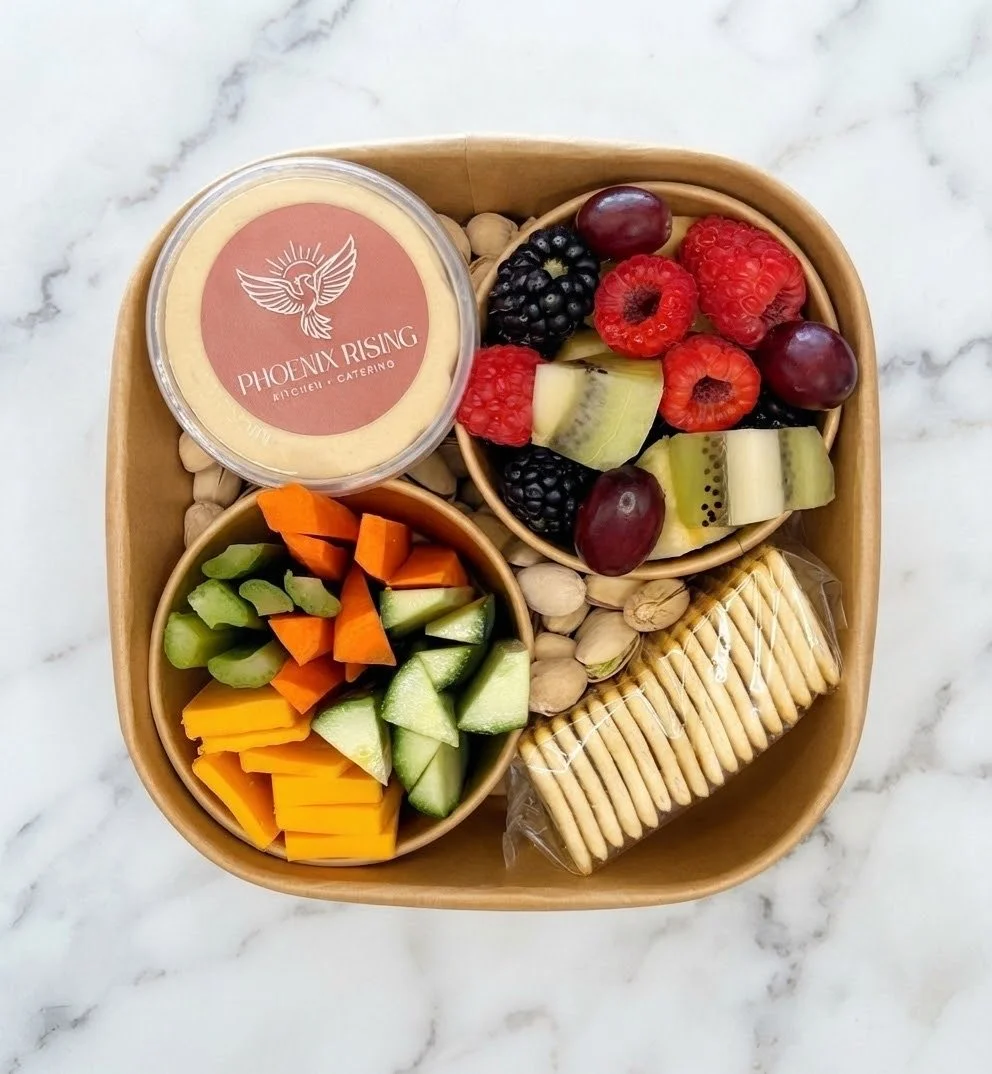 A container with mixed fresh fruits including strawberries, raspberries, blackberries, kiwi, red grapes, and cucumber slices, along with a small cup of cheese and a pack of crackers.