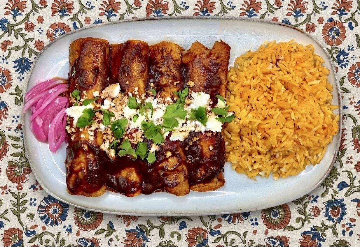 Plate of Mexican food featuring two types of enchiladas topped with sauce, garnished with cilantro, cheese, and crumbled topping, served with sliced red onions and rice