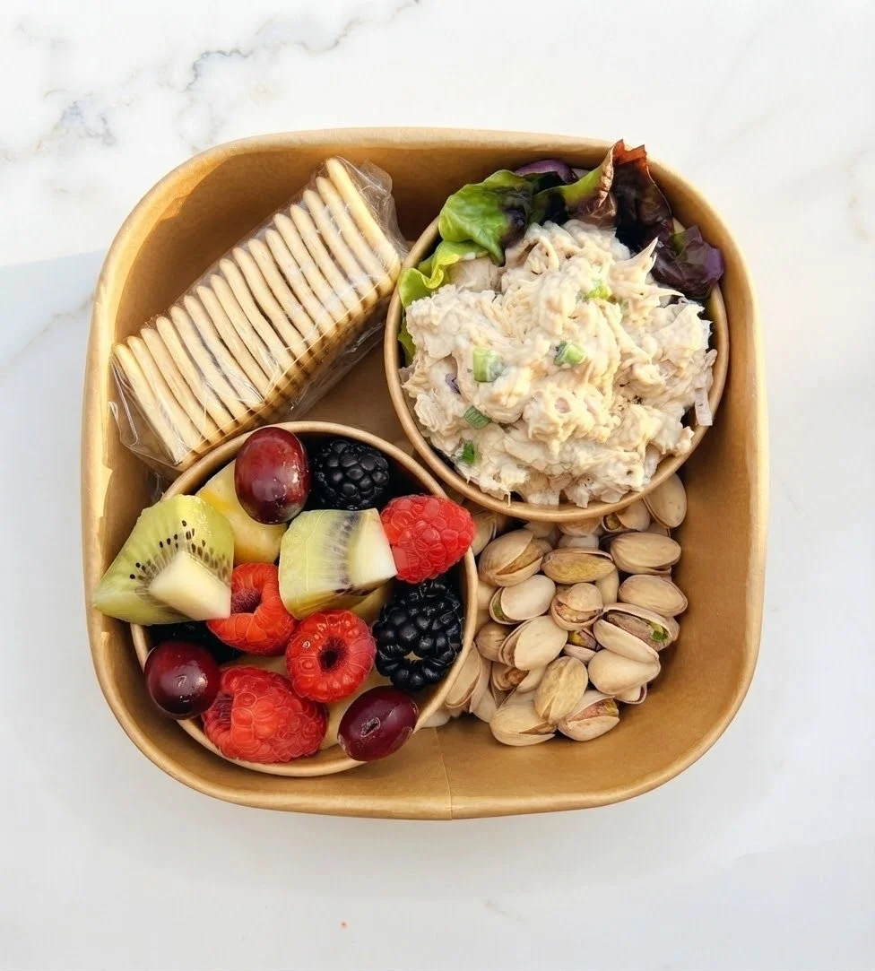 A tray with a serving of assorted snacks, including fresh fruit, a small bowl of potato salad, a stack of crackers, and a handful of pistachios.
