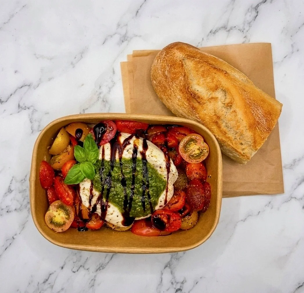 A bowl of Caprese salad with cherry tomatoes, fresh mozzarella, basil leaves, balsamic glaze, and olive oil, with a side of French bread on a marble surface.