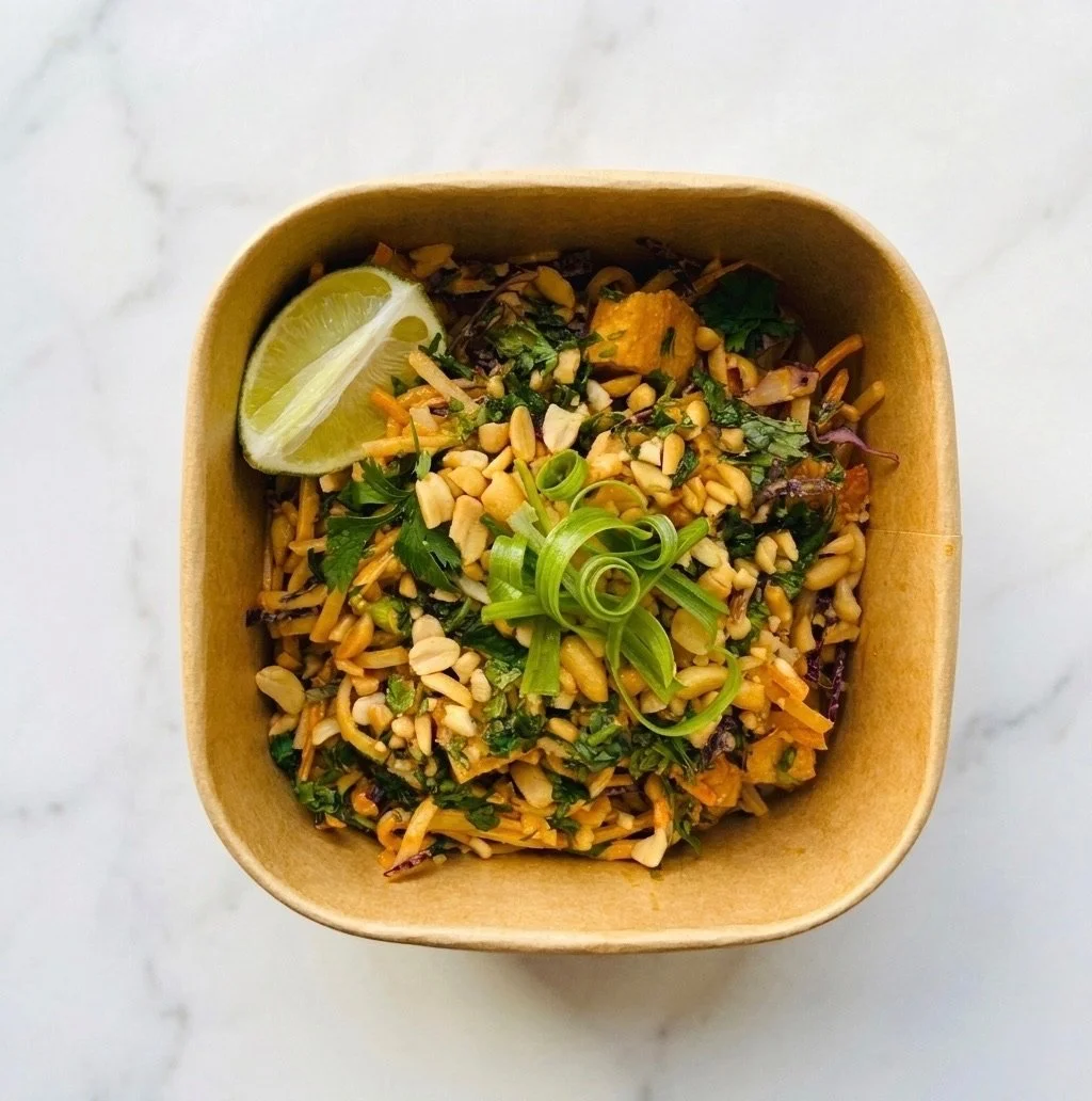 A bowl of Asian-style noodle salad garnished with chopped peanuts, sliced green onions, and a lemon wedge.