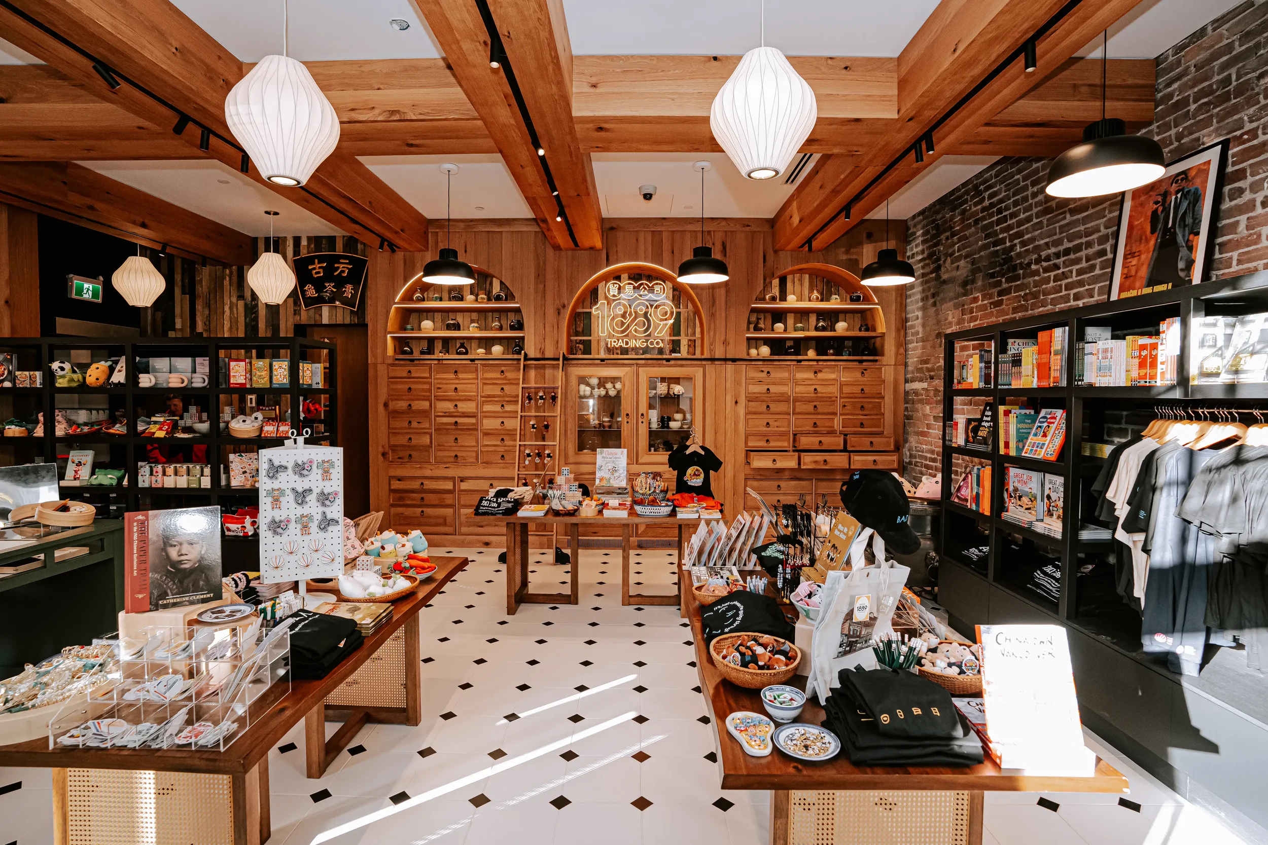 Interior of a retail store with wooden beams on the ceiling, black and brick walls, displaying various merchandise including books, accessories, and souvenirs organized on shelves and tables, with decorative lighting fixtures.