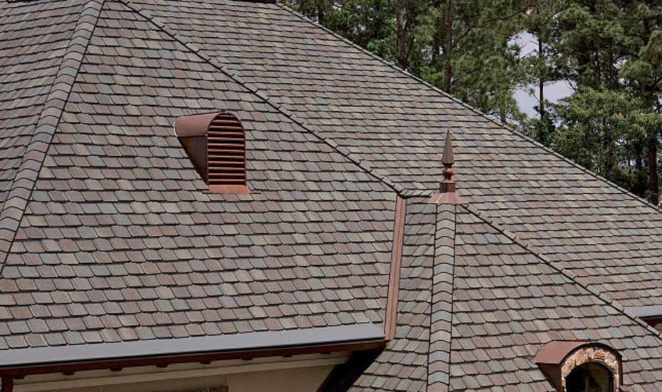Close-up of a shingled roof with vents and decorative spire, surrounded by trees.