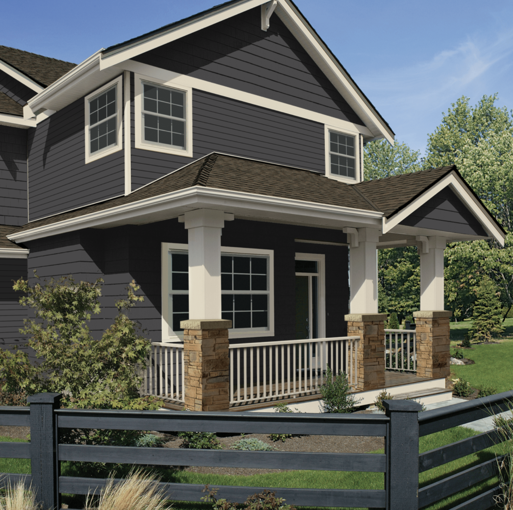 A two-story modern house with dark gray siding, white trim, a covered front porch with stone columns, a black wooden fence, and a landscaped yard with plants and trees.
