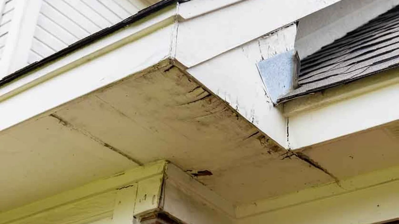 Close-up of a sagging porch roof with peeling paint and cracked wood on a house.