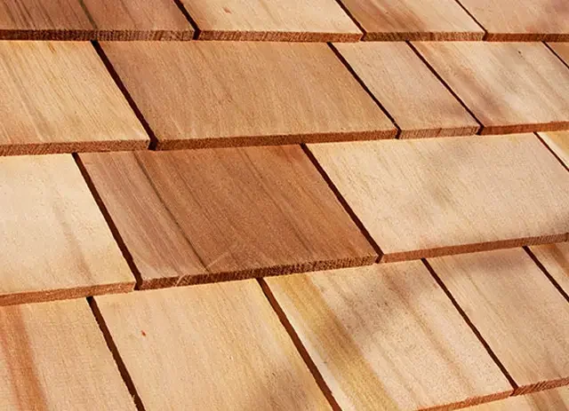 Close-up of a wooden shingle roof with overlapping rectangular tiles in various shades of light and dark brown.