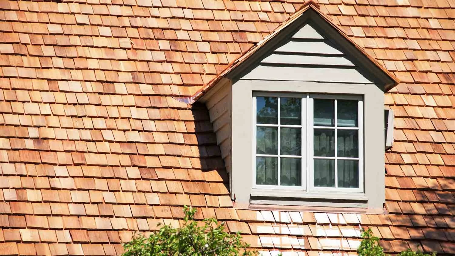Close-up of a house's roof with red clay shingles and a dormer window with white framing and divided panes.