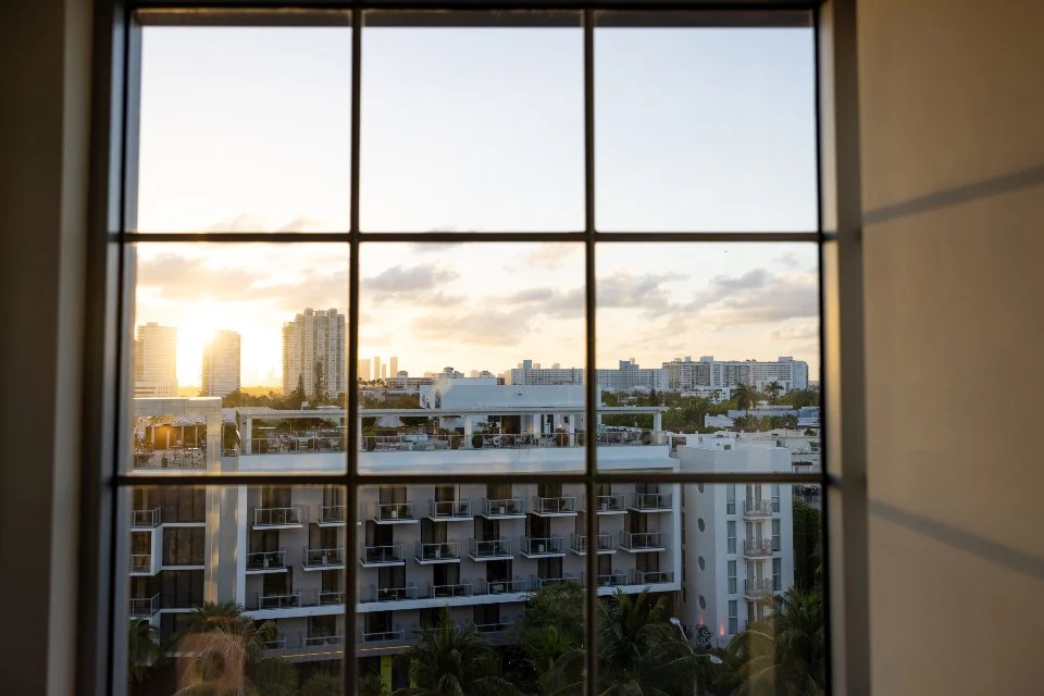 Sunset view through a window overlooking a cityscape with high-rise buildings and a modern apartment complex.