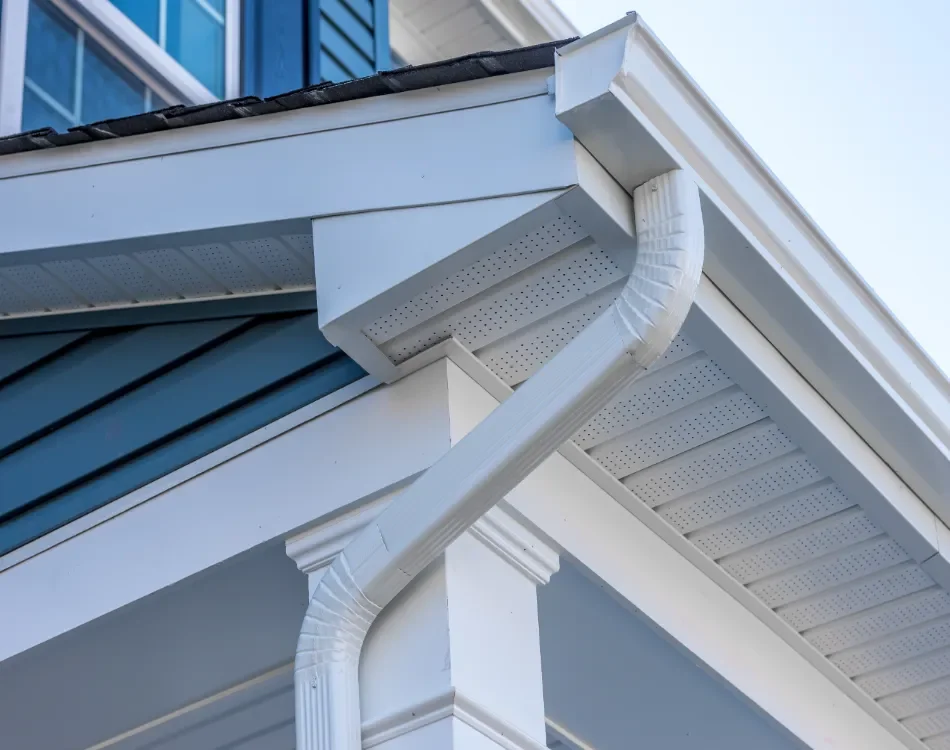 Close-up of house gutter system, showing downspout, drain, and roof edge with siding.