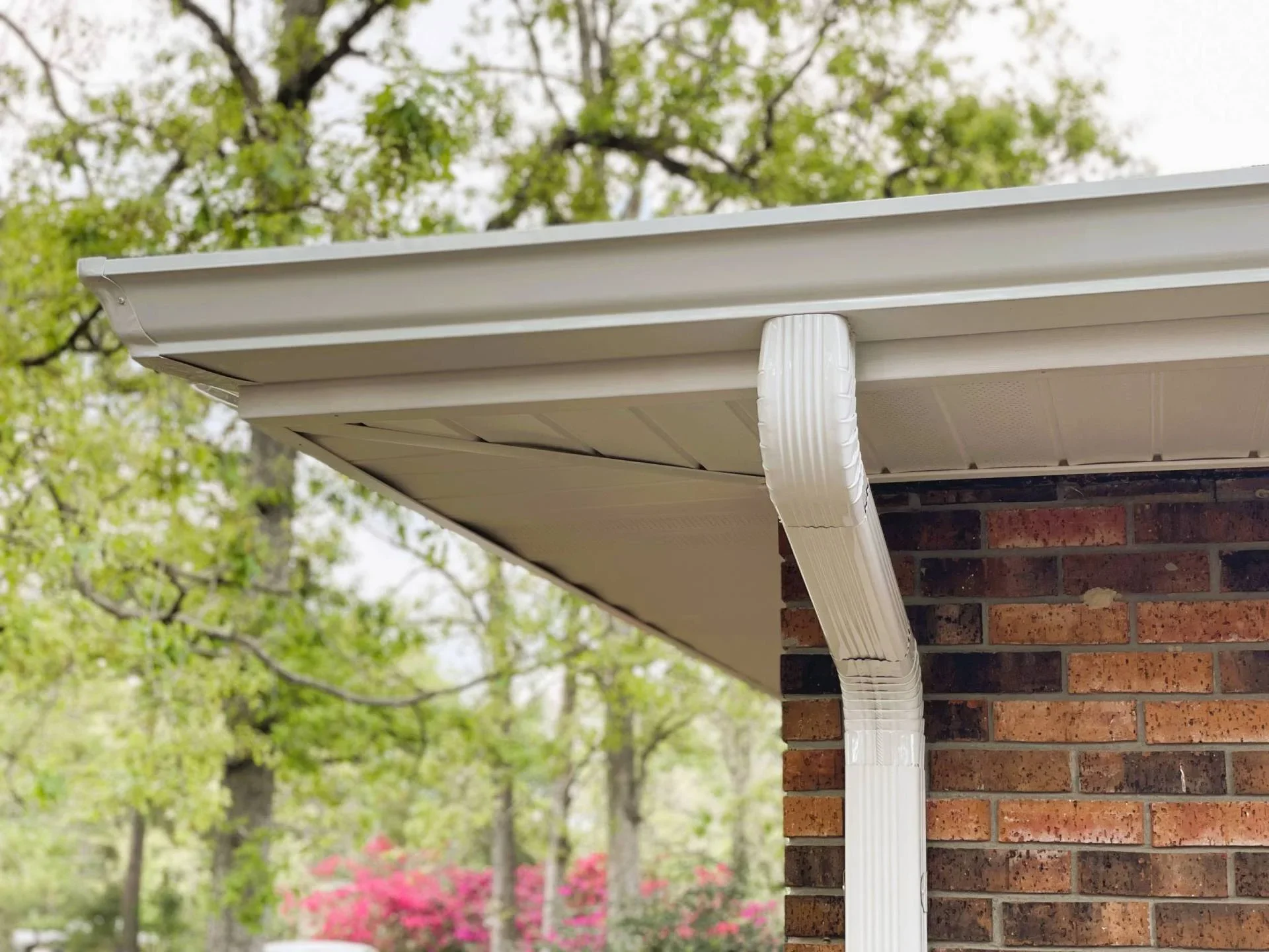Close-up of a house gutter and downspout on a brick house with trees in the background.