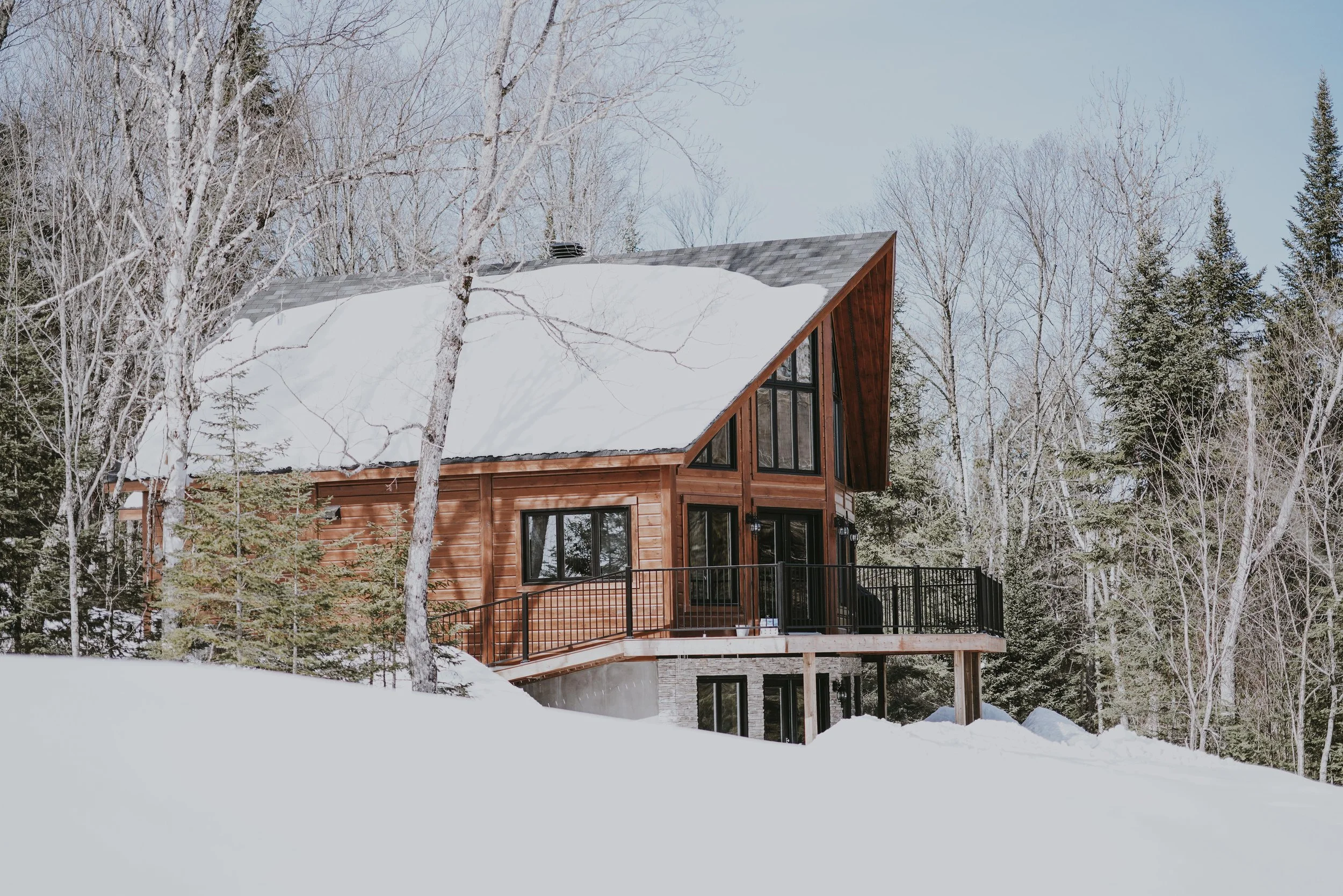 A wooden house with large windows in a snowy, forested area during winter.