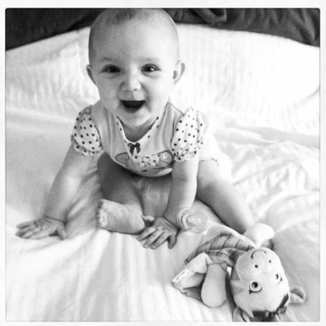 Smiling baby on bed with a plush toy