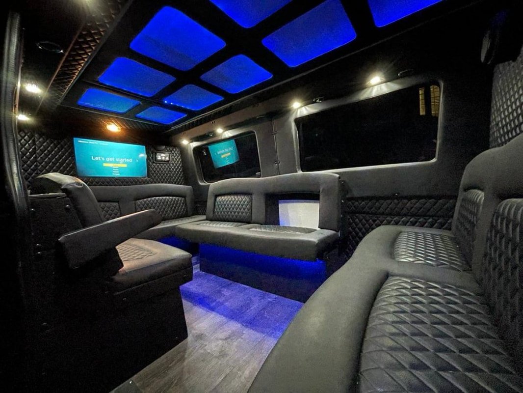 Interior of a luxury Sprinter Van with black quilted upholstery, LED lighting, and multiple windows.