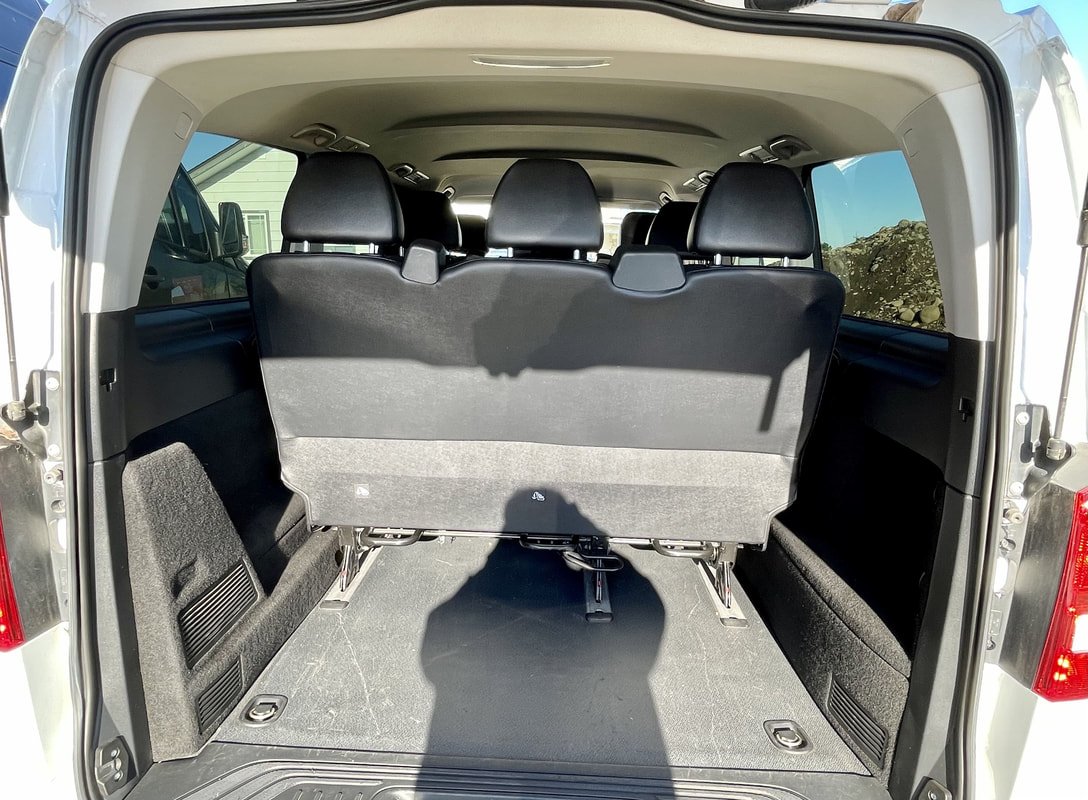 The trunk of a white SUV with the third-row seats folded down, showing a spacious cargo area with black carpeting and side storage compartments.