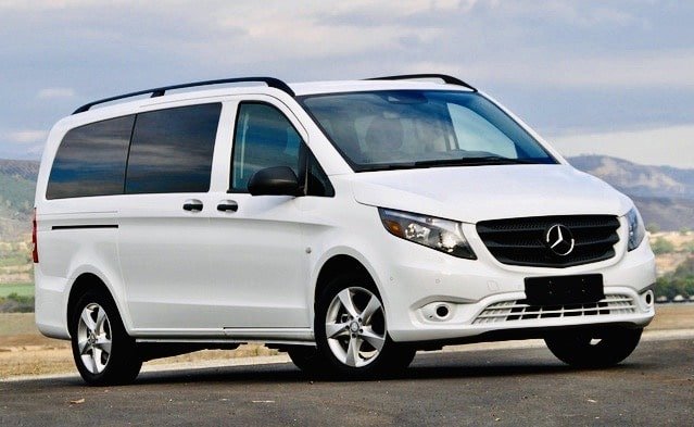 White Mercedes-Benz Metris van parked outdoors on a paved surface with a scenic background of mountains and cloudy sky.