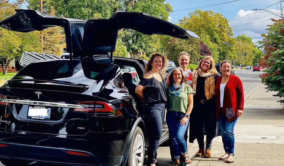 A wine tasting group of five women standing beside a black Tesla with its gullwing door open in Walla Walla.