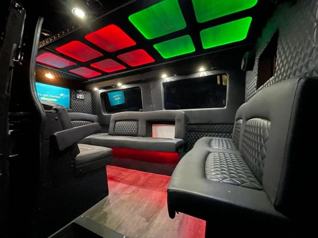 Luxury interior of a Sprinter Van with limo-style leather seating,  LED ceiling lights, and TV screens on the walls.