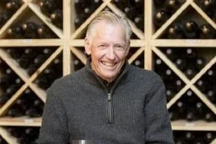 Norm McKibben standing in front of a wine rack filled with bottles.
