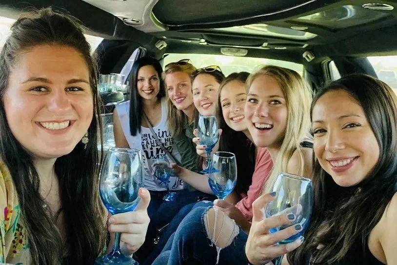 Wine tasting group of seven =women smiling and holding wine glasses inside a limo in the Walla Walla Valley.
