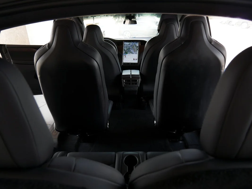 Interior of a Tesla with six black leather seats and a central touchscreen display on the dashboard.